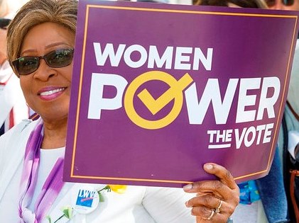 Woman Carrying Purple Sign That Says Women Power the Vote